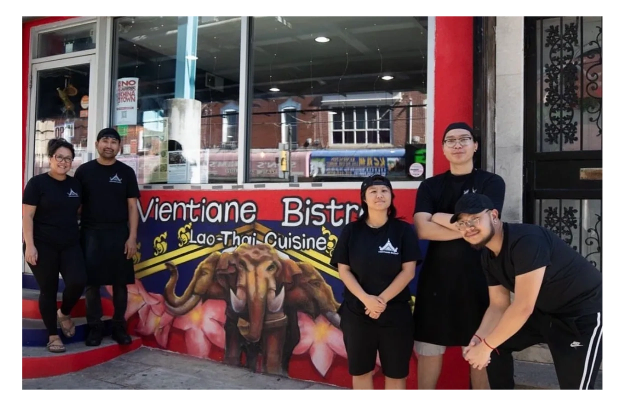 Five people in black shirts posing outside Vientiane Bistro, a Lao-Thai cuisine restaurant.