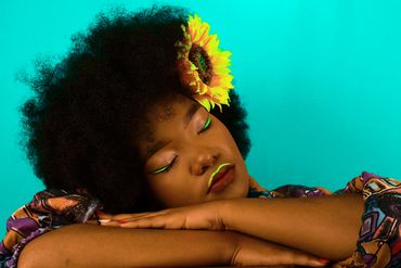 Woman with afro and sunflower resting peacefully with eyes closed.