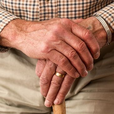 Elderly man's hands folded on top of cane.
