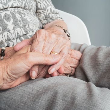 Person holding the hand of an elderly person, with hands folded on lap.
