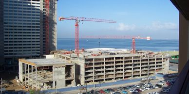 Construction site with cranes near a large body of water and parked cars.