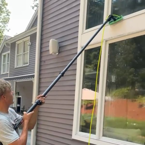 Man cleaning upper window using a long pole.