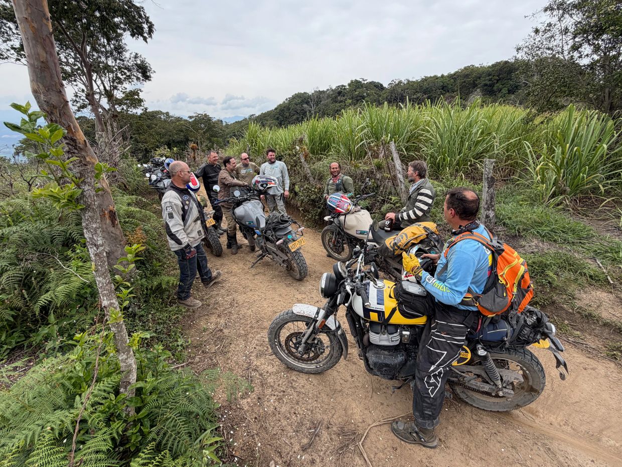 Group of motorcyclists chatting on a dirt road in a rural area.