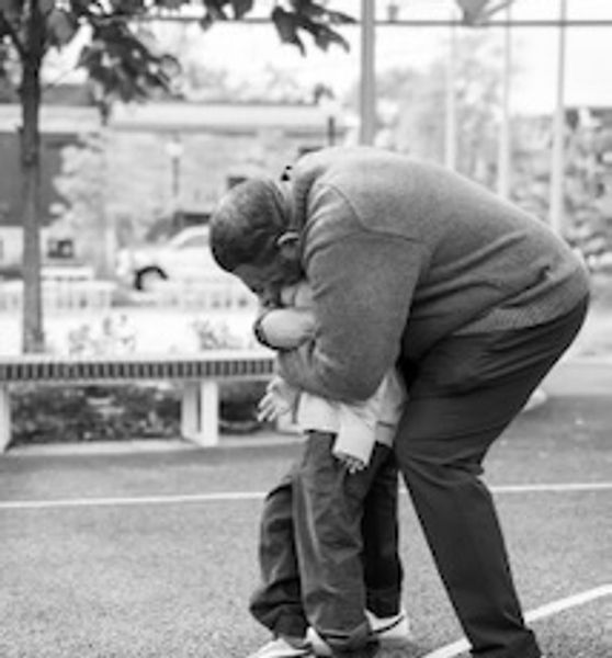A man lovingly hugs a child outdoors on a playground.