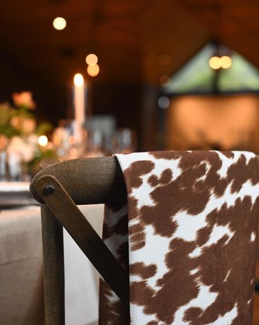 A cozy chair with a brown and white cowhide throw in a warm, softly lit dining room.