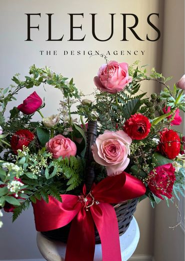 Elegant floral arrangement with pink and red roses in a basket adorned with a red bow.