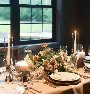 Elegant dinner table with floral centerpiece and lit candles by a window.