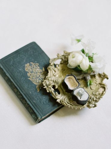 Vintage ring box with diamond ring on ornate tray and old book.