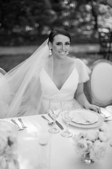 Bride in wedding dress sitting at a decorated table, smiling.