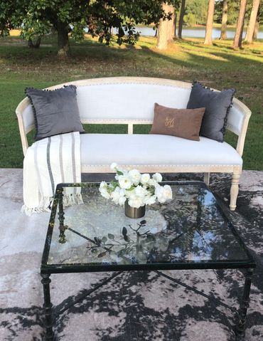 Elegant outdoor seating with a cushioned bench, decorative pillows, and a glass coffee table with flowers.