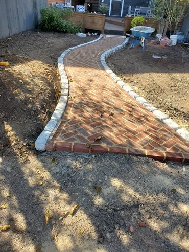 Curved brick pathway with stone edging in a backyard under renovation.