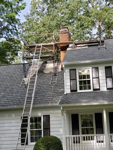 House roof under repair with scaffolding and ladders near chimney.