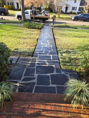 Newly installed stone walkway leading to the street with workers finishing up.