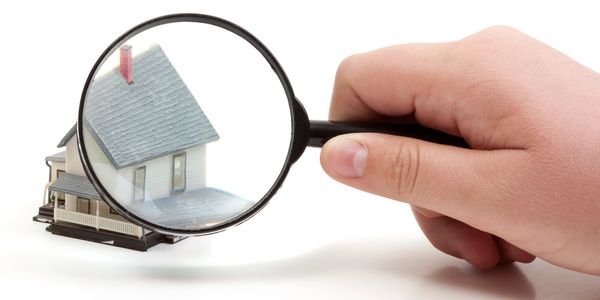 Hand holding magnifying glass over a miniature house model.