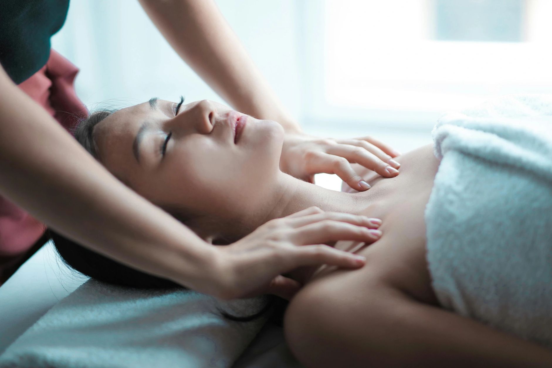 The woman receiving the massage is lying supine on a massage table covered off-white towel. Lymphatic Drainage Massage Mequon Milwaukee.