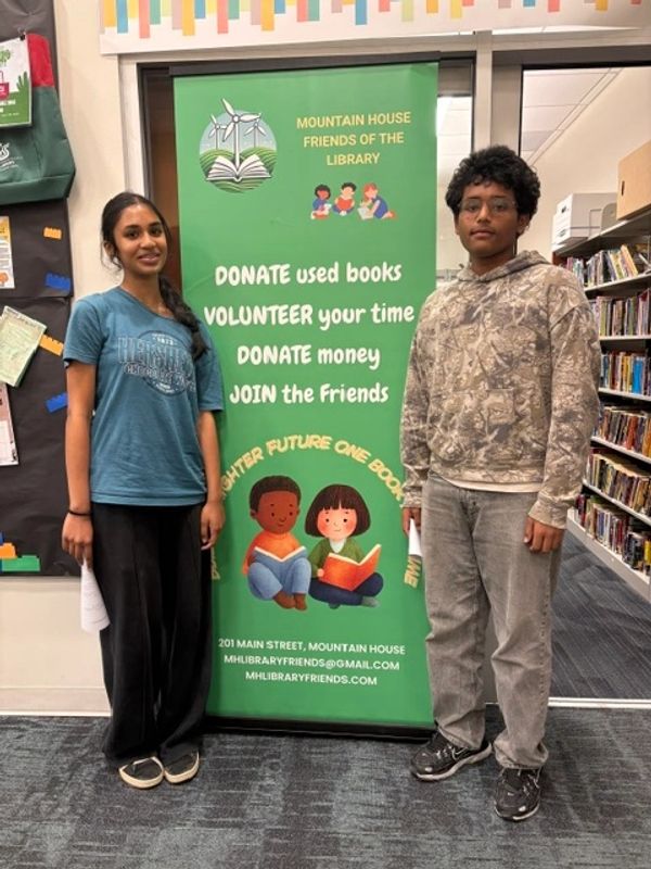 Two young people stand by a library volunteer sign.