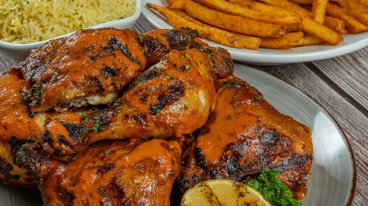 Flame grilled whole chicken on a plate with sided or basmati house rice and peri peri fires.