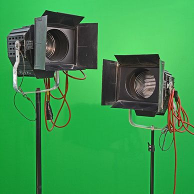 Two vintage studio lights with barn doors on stands, set against a green screen background.