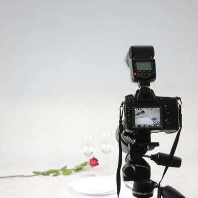 Camera setup for food photography with a rose and wine glasses in the background.