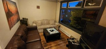 Cozy living room with brown and beige sofas, wooden floor, and large window at dusk.
