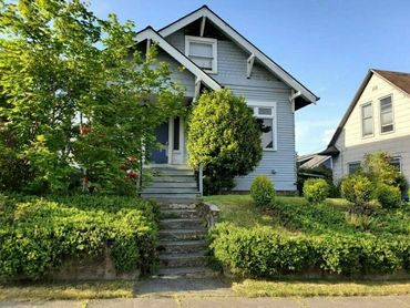 A quaint blue house surrounded by lush greenery and shrubs on a sunny day.