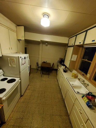 Vintage kitchen with patterned floor, white appliances, and wooden dining set under warm lighting.