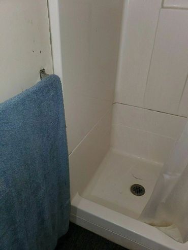 Small white shower stall with blue towel and some wear marks.