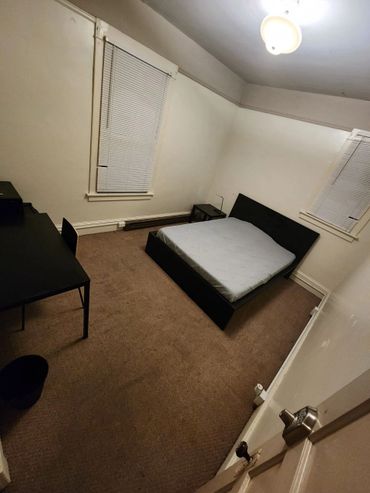 Spartan bedroom with basic furniture and closed blinds.