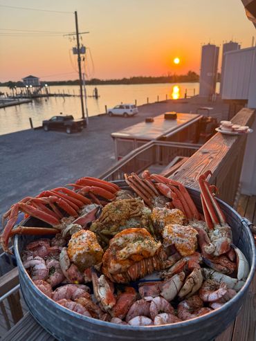 A seafood feast with crab legs and corn at sunset by the water.