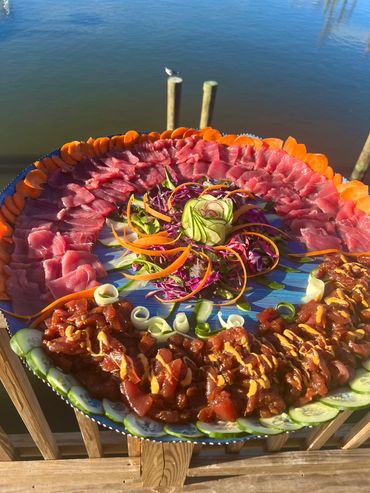 A beautifully arranged platter of sashimi and poke with fresh vegetables by the water.