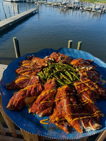 A blue plate with seasoned fish fillets and green beans by the water.