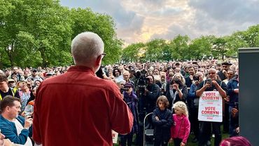 Man speaking to a large crowd at an outdoor event during sunset.