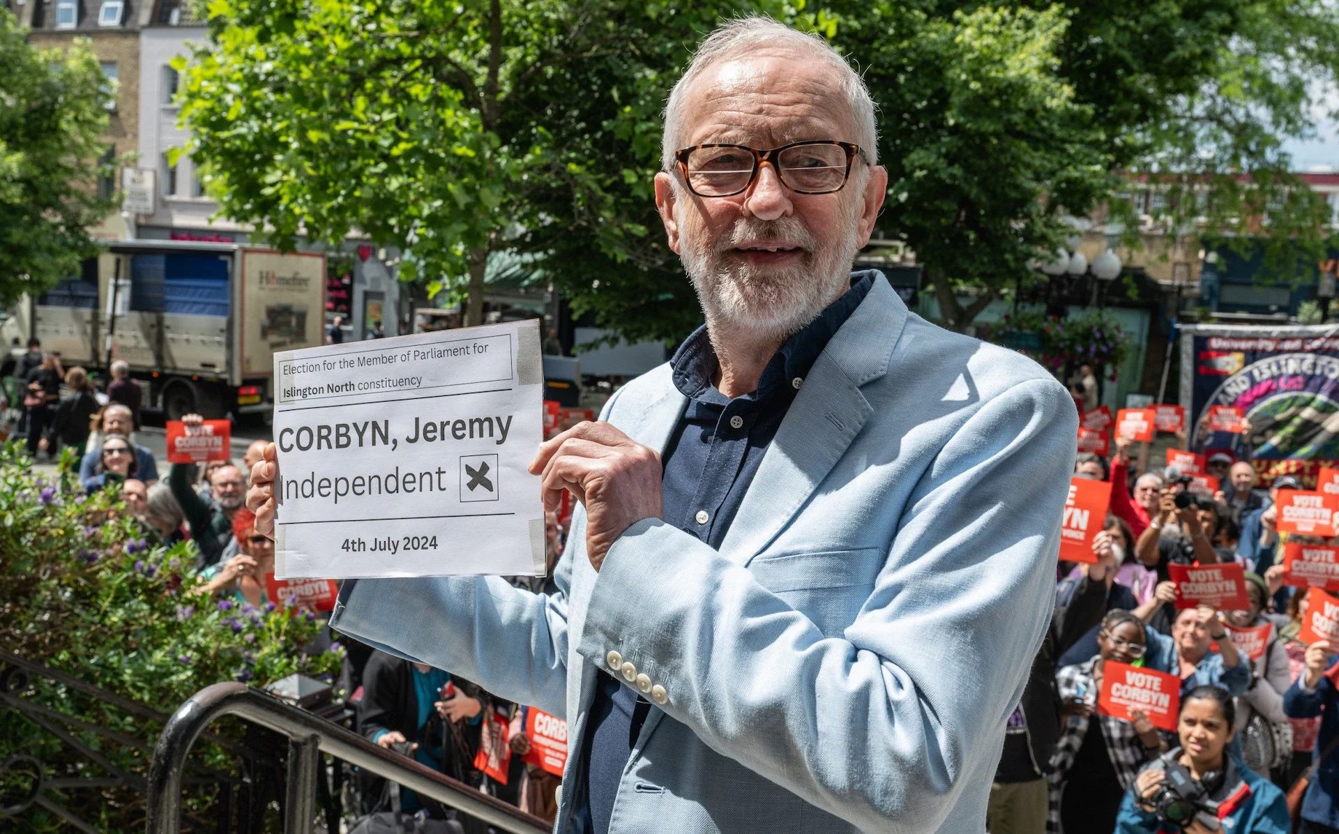 Jeremy Corbyn holds election sign for Islington North, supported by a crowd.