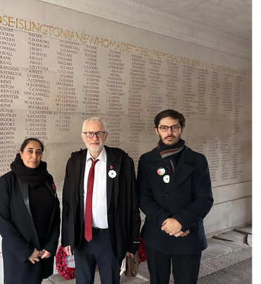 Three individuals standing solemnly in front of a war memorial wall.