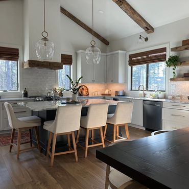Modern kitchen with wooden beams, white cabinets, and a large island with beige chairs.