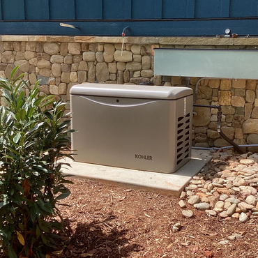 KOHLER backup generator installed outdoors near a stone wall.