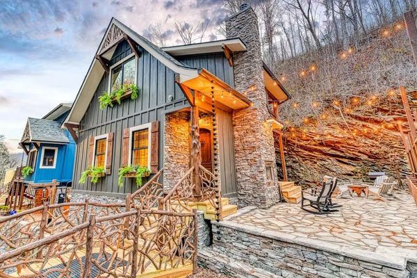 Cozy stone and wood cabin with outdoor seating and string lights in a wooded area.