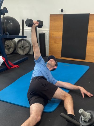 Man doing an exercise with a dumbbell on a blue mat.