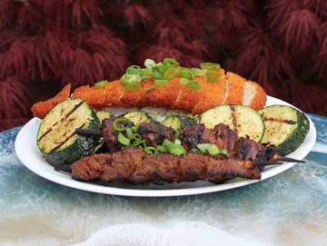 Grilled meat, zucchini, and fish on a plate.