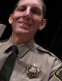 A smiling police officer in uniform with a badge and tie.