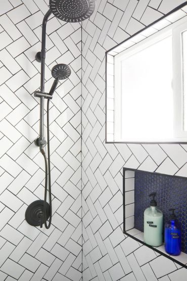 Modern shower with black fixtures and white herringbone tiles.