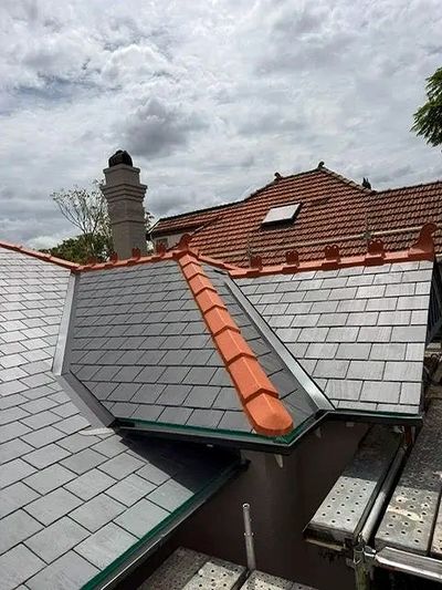 Newly installed slate roof with red ridge tiles under a cloudy sky.