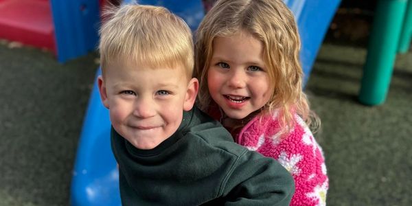 Two smiling children with blonde hair at a playground.