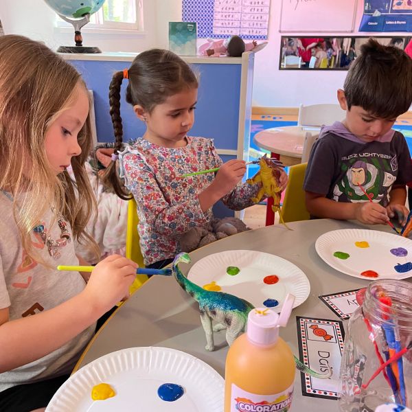 Children painting dinosaur toys at a table.