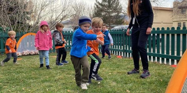 Children playing soccer outdoors with an adult.