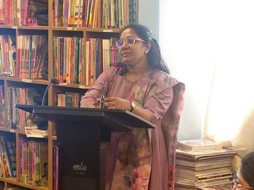 Woman speaking at a podium in a library setting.