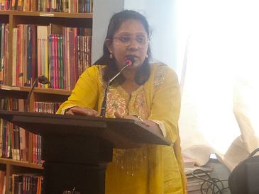 Woman in yellow speaking at a podium in a library.