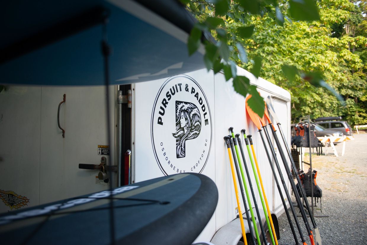 Paddleboards and paddles outside a Pursuit & Paddle trailer.