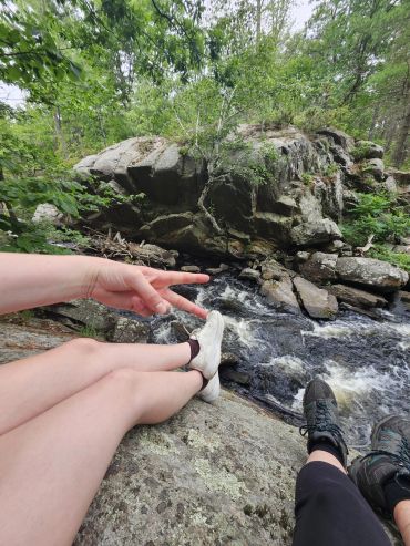 Relaxing by the river with peace sign and sneakers visible.