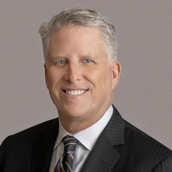 Professional portrait of a middle-aged man in a suit and tie smiling.